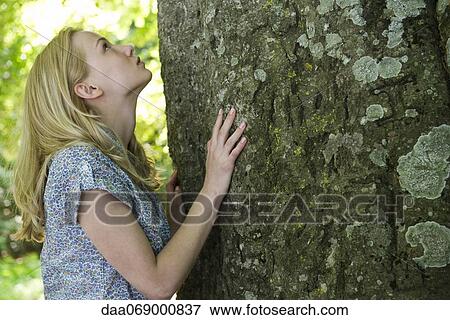 Stock Photo - Young woman looking up at tree. Fotosearch
