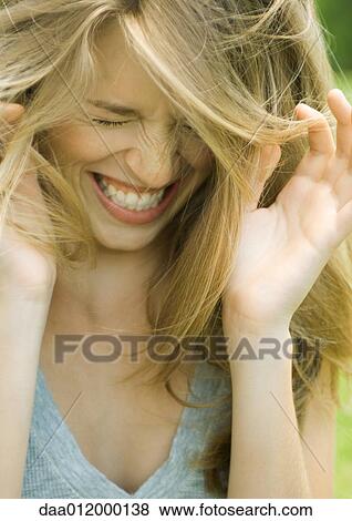 Stock Photo - Young woman lowering head, shutting eyes and laughing with hands up. Fotosearch