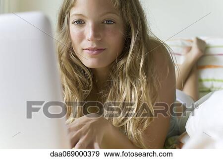 Young woman lying in bed, using laptop computer View Large Photo Image Stock Photo - Young woman lying in bed, using laptop computer. Fotosearch