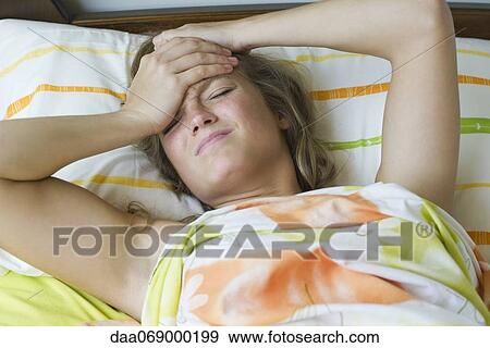 Young woman lying in bed with a headache View Large Photo Image Stock Photo - Young woman lying in bed with a headache. Fotosearch
