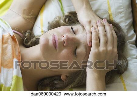 Young woman lying in bed with hands clasped on forehead View Large Photo Image Stock Photo - Young woman lying in bed with hands clasped on forehead. Fotosearch