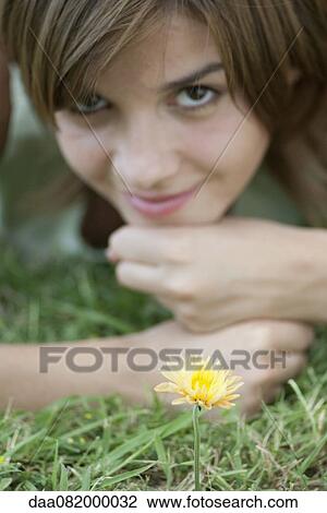 Stock Image - Young woman lying in grass by yelllolw flower. Fotosearch