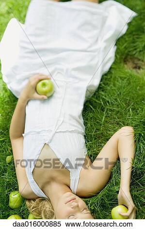 Young woman lying in grass, holding apples View Large Photo Image Stock Photography - Young woman lying in grass, holding apples. Fotosearch
