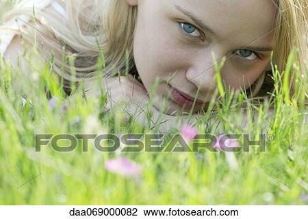 Stock Image - Young woman lying in grass, portrait. Fotosearch