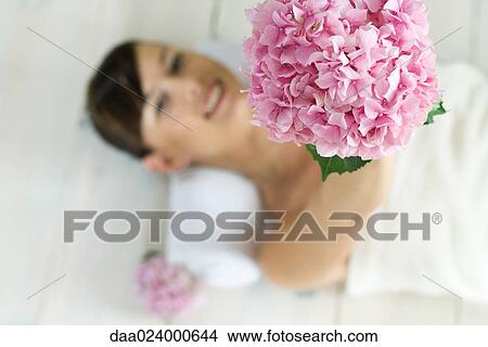 Young woman lying on back, holding up flower, view from directly above View Large Photo Image Picture - Young woman lying on back, holding up flower, view from directly above. Fotosearch