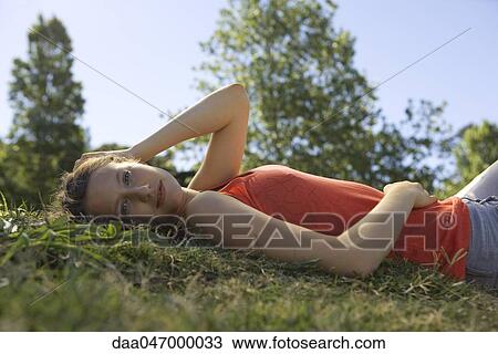 Stock Image - Young woman lying on back in grass, portrait. Fotosearch