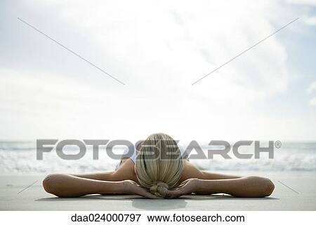 Young woman lying on back on beach with hands behind head, surface level view View Large Photo Image Stock Photo - Young woman lying on back on beach with hands behind head, surface level view. Fotosearch