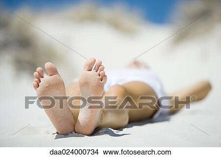 Young woman lying on beach, focus on feet in foreground View Large Photo Image Picture - Young woman lying on beach, focus on feet in foreground. Fotosearch