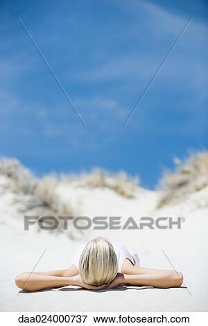Young woman lying on beach, hands behind head View Large Photo Image Stock Photo - Young woman lying on beach, hands behind head. Fotosearch