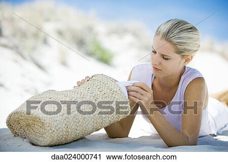 Young woman lying on beach, looking through beach bag View Large Photo Image Stock Image - Young woman lying on beach, looking through beach bag. Fotosearch