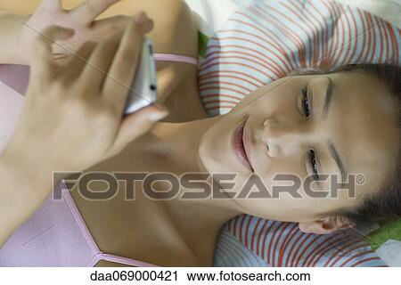 Young woman lying on bed text messaging View Large Photo Image Stock Image - Young woman lying on bed text messaging. Fotosearch