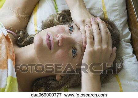 Young woman lying on bed with hands clasped on forehead, looking up in thought View Large Photo Image Stock Photo - Young woman lying on bed with hands clasped on forehead, looking up in thought. Fotosearch