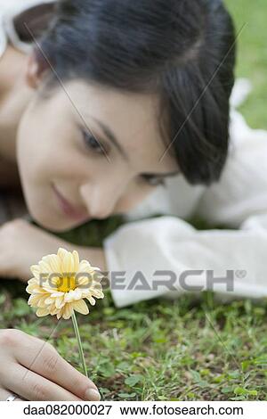 Young woman lying on grass looking at yellow flower View Large Photo Image Stock Photo - Young woman lying on grass looking at yellow flower. Fotosearch