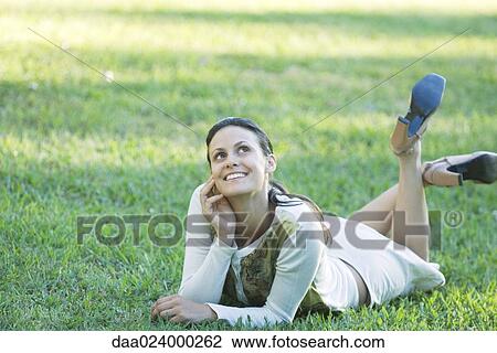 Stock Image - Young woman lying on grass, looking up. Fotosearch