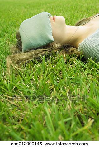 Stock Photography - Young woman lying on grass with eye pillow covering eyes. Fotosearch