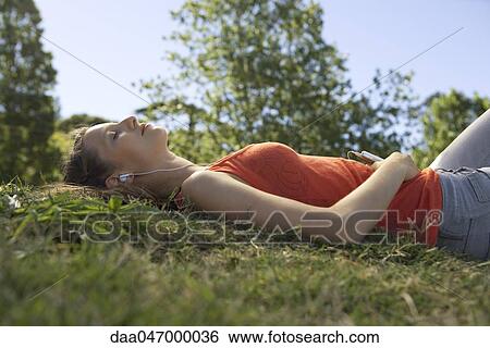Young woman lying on ground listening to MP3 player, eyes closed View Large Photo Image Stock Photograph - Young woman lying on ground listening to MP3 player, eyes closed. Fotosearch