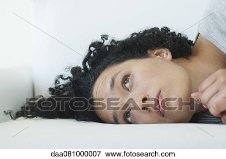 Stock Photo - Young woman lying on side, idly looking up. Fotosearch