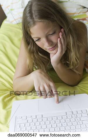 Young woman lying on stomach in bed, using laptop computer View Large Photo Image Stock Photo - Young woman lying on stomach in bed, using laptop computer. Fotosearch