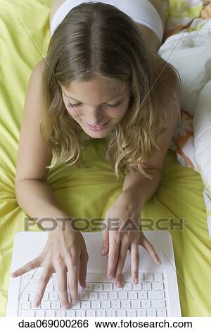 Young woman lying on stomach in bed, using laptop computer View Large Photo Image Stock Photograph - Young woman lying on stomach in bed, using laptop computer. Fotosearch