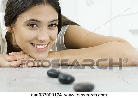 Young woman lying on stomach, resting head on arms, behind small black stones in a line View Large Photo Image Picture - Young woman lying on stomach, resting head on arms, behind small black stones in a line. Fotosearch