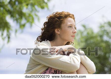 Stock Image - Young woman outdoors, looking away in thought. Fotosearch