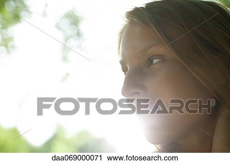 Stock Image - Young woman outdoors, looking away in thought. Fotosearch