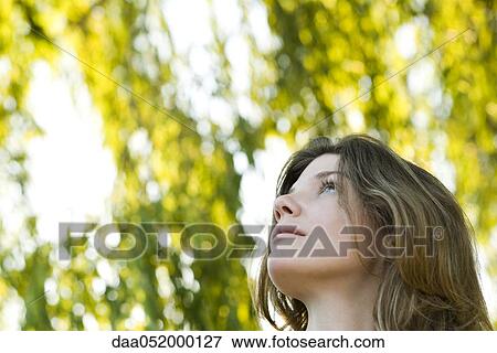 Stock Photo - Young woman outdoors, looking up, portrait. Fotosearch