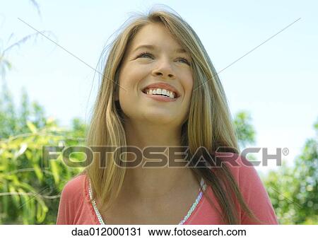 Stock Image - Young woman outdoors, smiling and looking up. Fotosearch