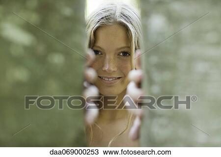 Young woman peering out from behind tree trunks View Large Photo Image Stock Image - Young woman peering out from behind tree trunks. Fotosearch