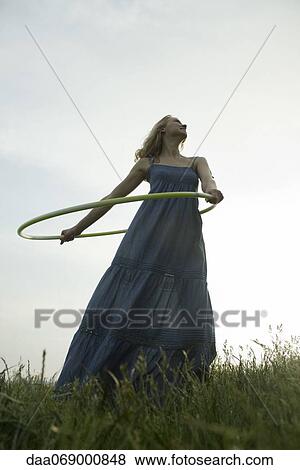 Stock Photo - Young woman playing with plastic hoop outdoors. Fotosearch