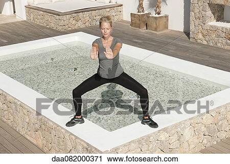 Stock Image - Young woman practicing tai chi chuan in patio with eyes closed. Fotosearch