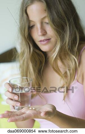Picture - Young woman preparing to take pills with glass of water. Fotosearch