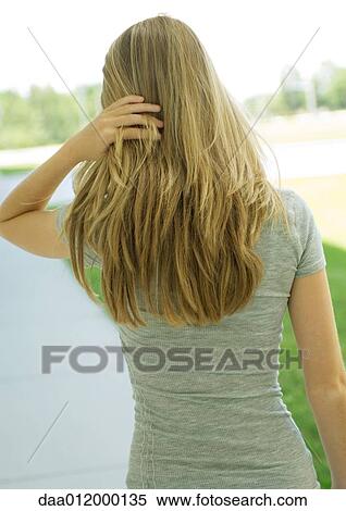 Stock Photography - Young woman pushing hair back, rear view, waist up. Fotosearch