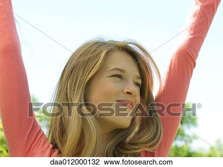 Young woman raising arms outdoors, smiling View Large Photo Image Stock Image - Young woman raising arms outdoors, smiling. Fotosearch