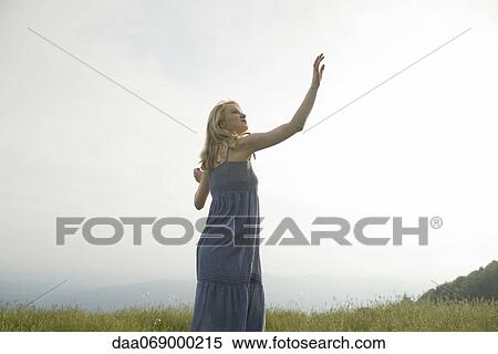Stock Photography - Young woman reaching to touch bubble floating above her head. Fotosearch
