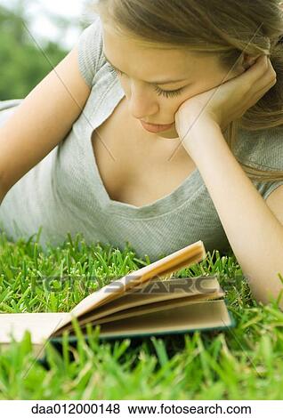 Young woman reclining in grass with book View Large Photo Image Stock Photo - Young woman reclining in grass with book. Fotosearch