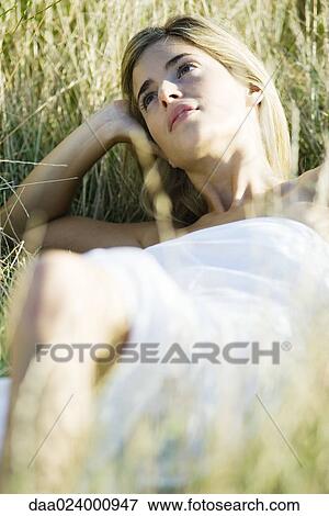 Young woman reclining in tall grass, holding head and looking away View Large Photo Image Stock Photo - Young woman reclining in tall grass, holding head and looking away. Fotosearch