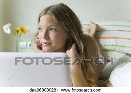 Young woman relaxing in bed with laptop computer, looking away dreamily View Large Photo Image Stock Photo - Young woman relaxing in bed with laptop computer, looking away dreamily. Fotosearch