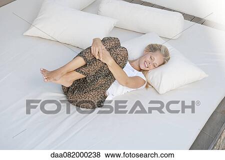 Stock Photo - Young woman relaxing on bed in fetal position. Fotosearch