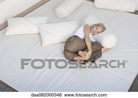 Stock Photo - Young woman relaxing on bed in fetal position. Fotosearch