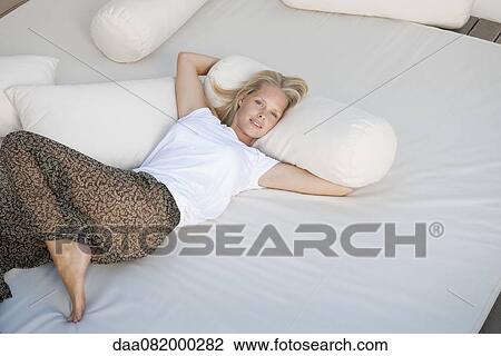 Stock Image - Young woman relaxing on bed. Fotosearch