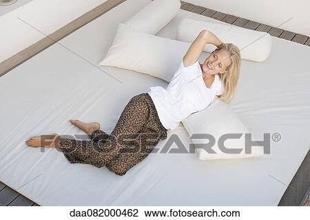Stock Image - Young woman relaxing on bed. Fotosearch