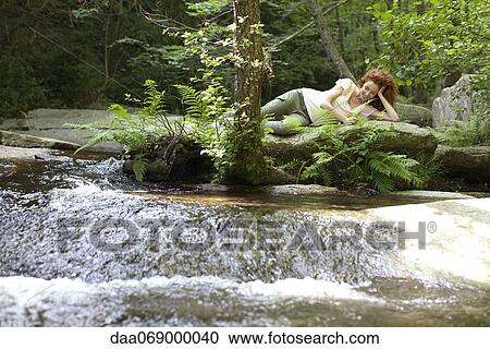 Young woman relaxing on rock by flowing stream View Large Photo Image Stock Image - Young woman relaxing on rock by flowing stream. Fotosearch