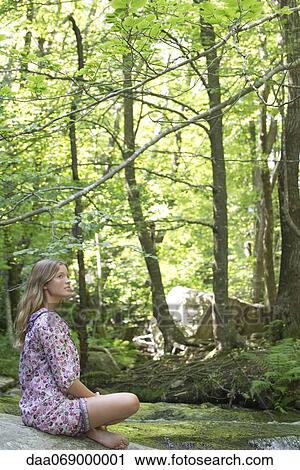 Stock Image - Young woman relaxing on rock in forest. Fotosearch