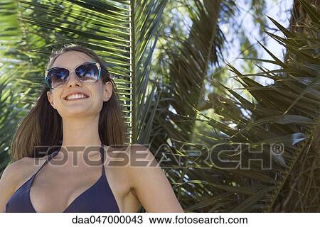 Young woman relaxing, wearing sunglasses, palm leaves in background View Large Photo Image Stock Image - Young woman relaxing, wearing sunglasses, palm leaves in background. Fotosearch