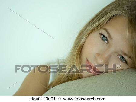 Stock Photo - Young woman resting head on cushion, looking at camera. Fotosearch