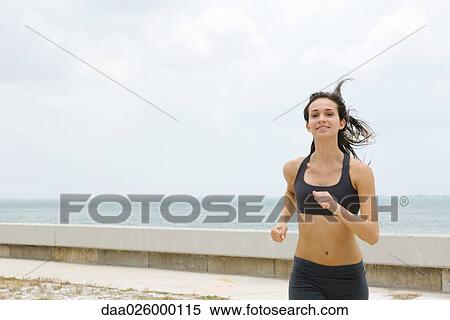 Young woman running at the beach, hair tousled, smiling View Large Photo Image Stock Photography - Young woman running at the beach, hair tousled, smiling. Fotosearch