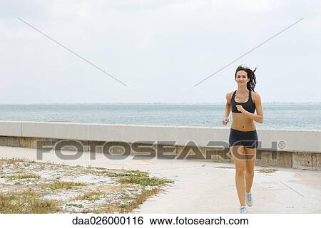 Young woman running at the beach, smiling at camera, full length View Large Photo Image Stock Photograph - Young woman running at the beach, smiling at camera, full length. Fotosearch