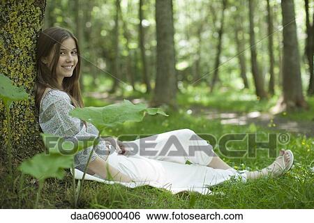 Young woman sitting against tree in woods, portrait View Large Photo Image Stock Photograph - Young woman sitting against tree in woods, portrait. Fotosearch