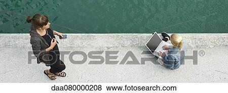 Stock Photo - Young woman sitting beside canal, using laptop computer, elevated view. Fotosearch